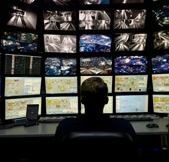 A man seated at a desk, focused on a large monitor displaying multiple screens with various data and graphics.