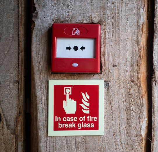 Bright red fire alarm sign affixed to a wooden wall, signaling the presence of fire safety equipment.