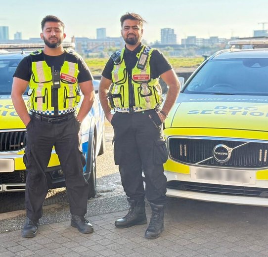 Two men in vests stand next to a police vehicle, indicating a professional or official interaction.